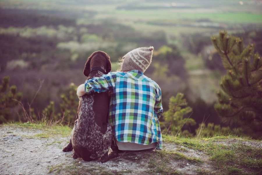 Eine Person sitzt mit ihrem Hund in der Natur, Rückansicht
