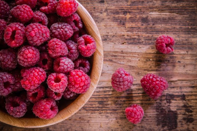 Himbeeren sind besonders ballaststoffreich und somit super für den Darm. Himbeeren in Holzschale auf einem Holztisch.