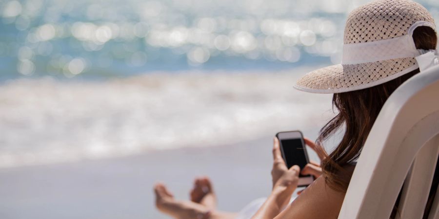 Junge Frau mit Handy am Strand.