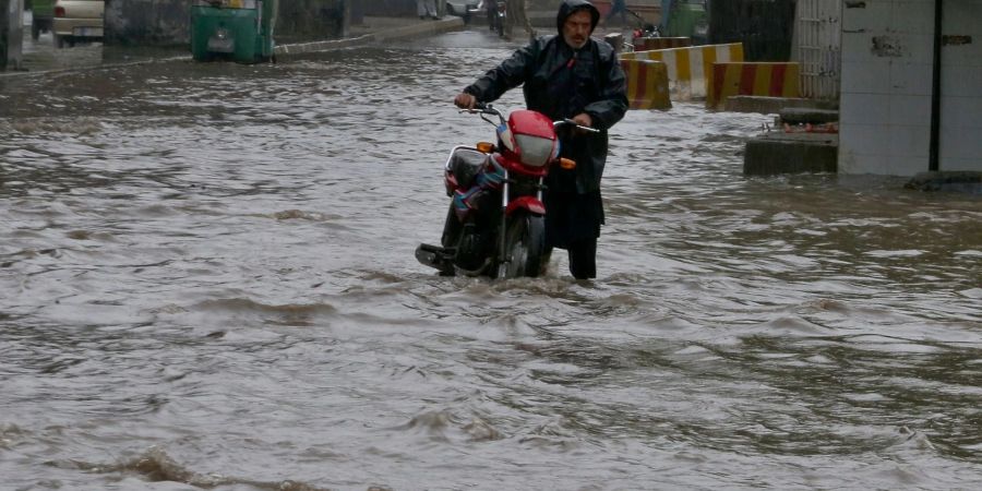 Ein Pakistaner watet nach starken Regenfällen mit seinem Motorrad durch eine überschwemmte Strasse in Peschawar.