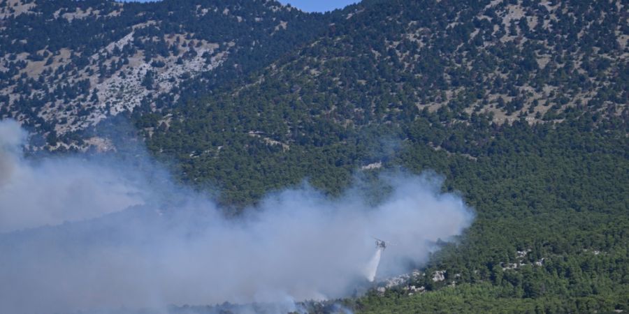 dpatopbilder - Ein Löschhubschrauber wirft bei einem Waldbrand nordwestlich von Athen Wasser über einem rauchverhangenen Wald ab. Foto: Michael Varaklas/AP/dpa