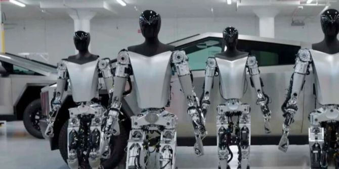 Unternehmensfoto mehrere Optimus Roboter vor einem Tesla