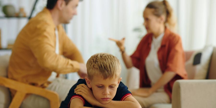 Trauriger Junge, im Hintergrund diskutieren die Eltern