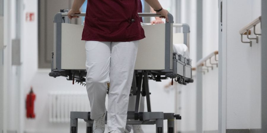 Eine Krankenpflegerin und ein Krankenpfleger schieben ein Krankenbett durch den Gang einer Station eines Krankenhauses. +++ dpa-Bildfunk +++