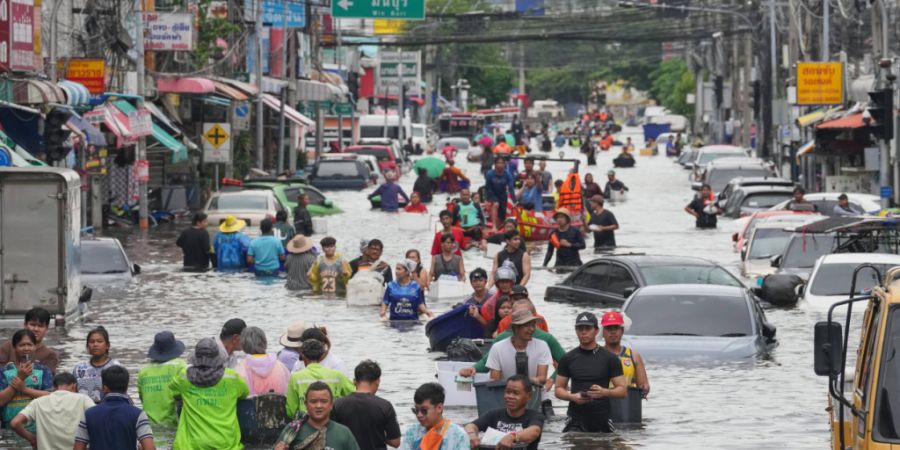 Menschen waten nach starken Regenfällen in der thailändischen Hauptstadt durch eine überflutete Straße. Foto: Sakchai Lalit/AP/dpa