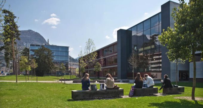 Studenten auf der Wiese vor der Bibliothek auf dem Universitätscampus in Lugano. Lugano Universitätscampus