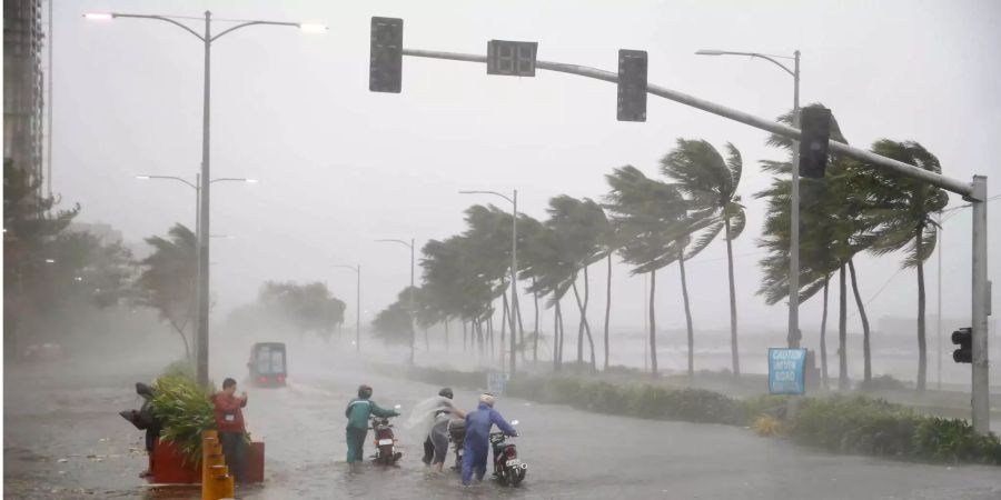 Verkehrsteilnehmer schieben während heftiger Regenfälle und starken Winden, die durch den Taifun «Mangkhut» verursacht wurden, ihre Motorroller über eine überflutete Strasse.