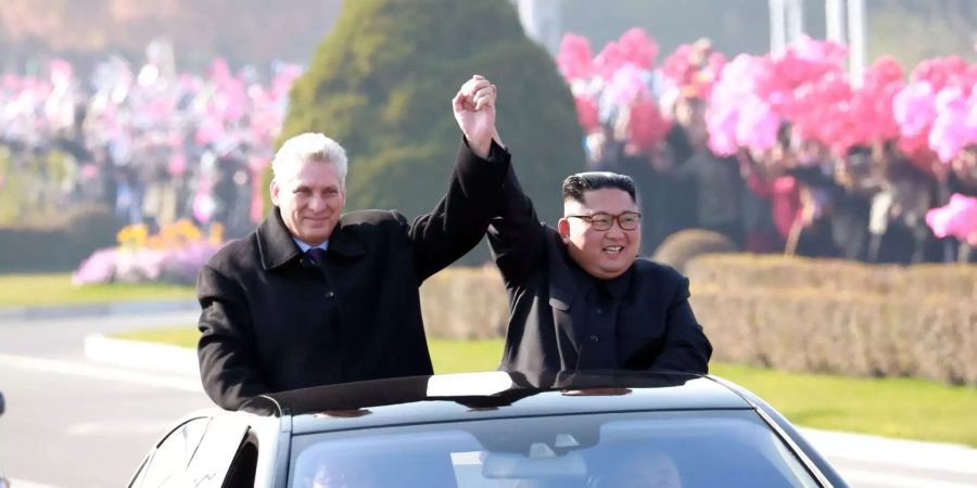 Kim Jong Un (r), Machthaber in Nordkorea, und Miguel Diaz-Canel, Präsident von Kuba, heben in einer Limousine stehend die Arme.