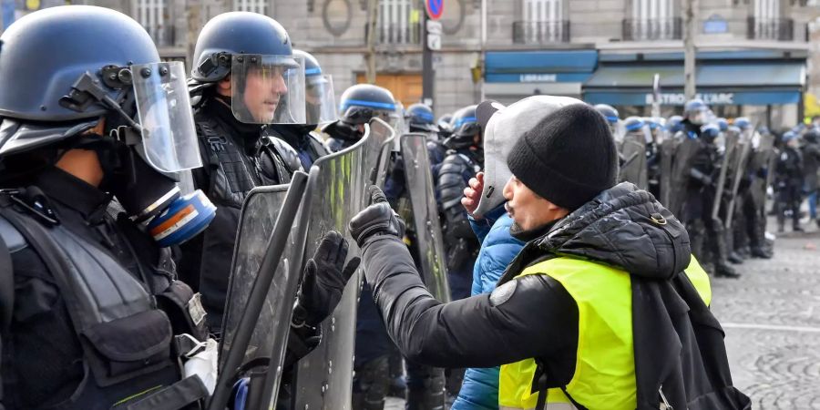 Ein Demonstrant in einer gelben Warnweste spricht zu Polizisten.