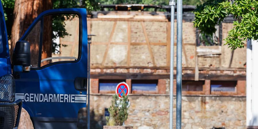 Die Tür eines Fahrzeugs der Gendarmerie steht offen, während im Hintergrund ein Haus zu sehen ist, in dem am Vortag bei einem Feuer elf Menschen ums Leben kamen. Nach dem Brand in der Ferienunterkunft im Elsass dauern die Ermittlungen zur Brandursache an. Foto: Philipp von Ditfurth/dpa