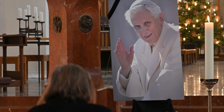 Eine Frau betet in der Frauenkirche in München vor einem Bild des verstorbenen emeritierten Papst Benedikt XVI.