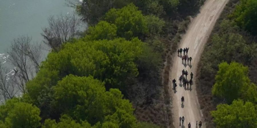 Migranten gehen einen Feldweg in Mission (Texas) entlang, nachdem sie die Grenze zwischen Mexiko und den USA überquert haben. Foto: Julio Cortez/AP/dpa