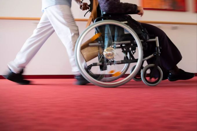 Ein Pfleger eines Pflegeheims schiebt eine Bewohnerin mit einem Rollstuhl. (Symbolbild) Pflegeheim