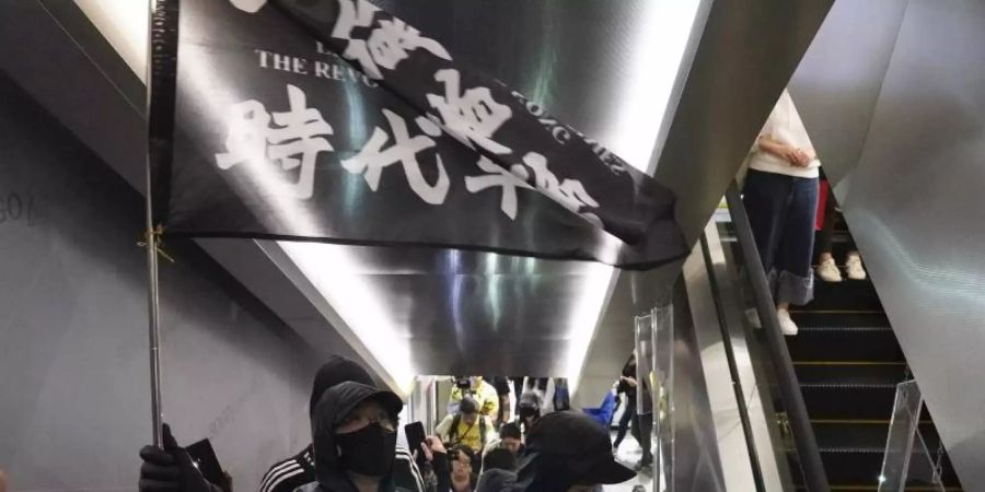 Demonstranten mit Mundschutz tragen eine Flagge mit der Aufschrift «Befreit Hongkong, die Revolution unserer Zeit» in einem Einkaufszentrum. Foto: Vincent Yu/AP/dpa