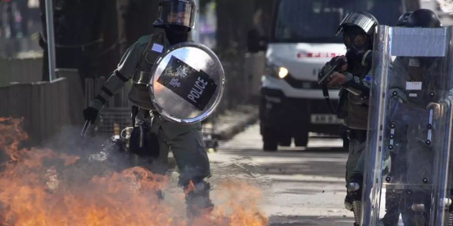 Ein Molotow-Cocktail geht vor Polizisten in Flammen auf. Foto: Ng Han Guan/AP/dpa