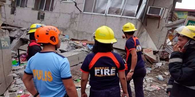 Anwohner und Rettungskräfte stehen neben einem zerstörten Gebäude. Philippinen starkes erdbeben