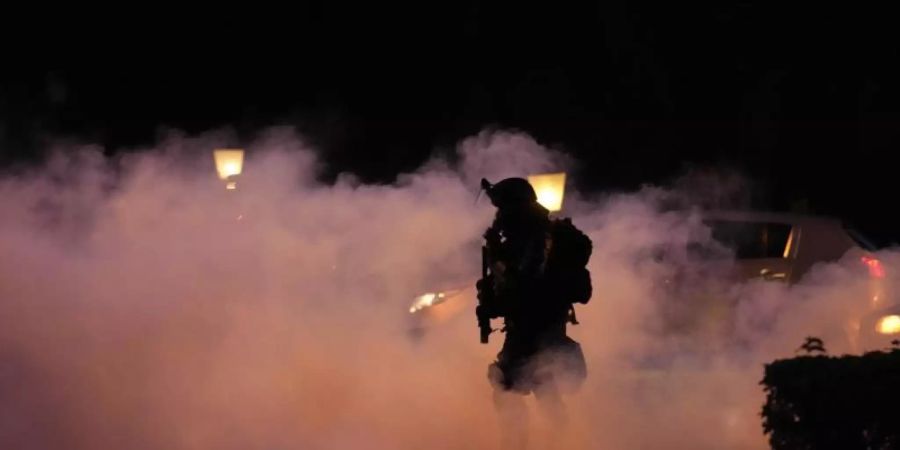 Ein Polizist geht durch Rauch während einer Demonstration gegen Corona-Impfungen in Ljubljana. Foto: Petr David Josek/AP/dpa