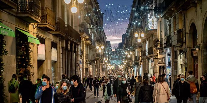 Menschen gehen eine beleuchtete Strasse in Barcelona entlang. Trotz einer hohen Impfquote von rund 80 Prozent klettert auch in Spanien die Zahl der Corona-Infektionen weiter rasant. Foto: Jordi Boixareu/ZUMA Press Wire/dpa spanien
