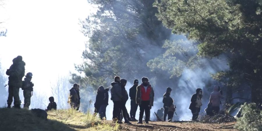 Belarussische Soldaten (l) stehen Wache, während sich Migranten an der belarussisch-polnischen Grenze versammeln. Foto: Leonid Shcheglov/BelTA/AP/dpa