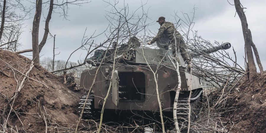 Ein ukrainischer Soldat verdeckt einen Schützenpanzer im Donbass mit Ästen.