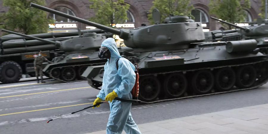 dpatopbilder - Ein städtischer Angestellter, der einen Spezialanzug zum Schutz gegen das Coronavirus trägt, desinfiziert einen Bereich, während sich sowjetische Panzer T-34 aus dem Zweiten Weltkrieg auf eine Probe für die Foto: Alexander Zemlianichenko/AP/dpa