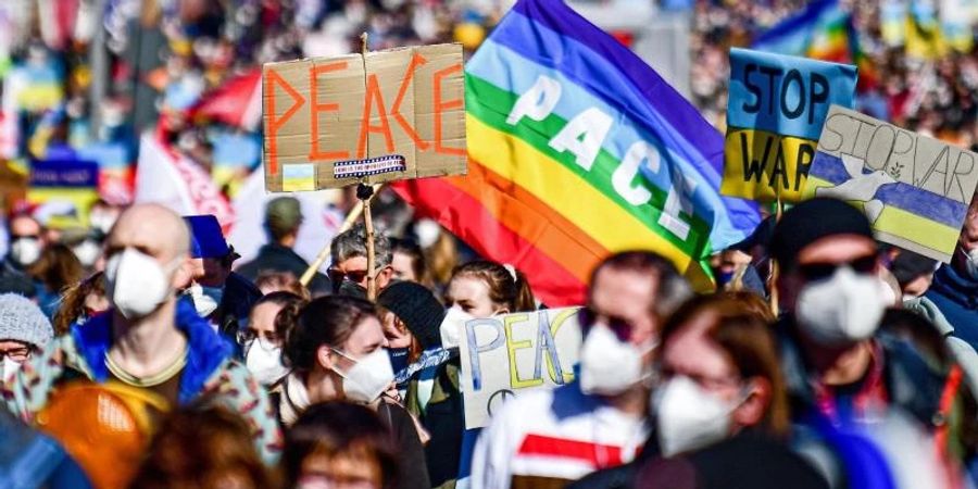 Menschen halten «Peace»-Schilder hoch, während sie an einer Friedensdemonstration gegen den Krieg in der Ukraine protestieren. Foto: Fabian Sommer/dpa