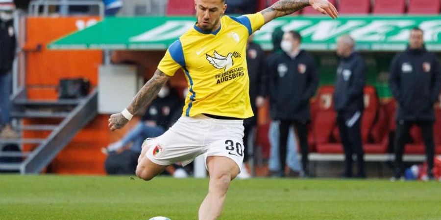 Augsburgs Niklas Dorsch wärmt sich in einem Trikot in den Landesfarben der Ukraine auf. Foto: Matthias Balk/dpa