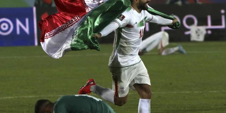 Der Iraner Saman Ghoddoos läuft nach dem Sieg im Azadi Stadion mit einer Fahne über das Spielfeld. Foto: Vahid Salemi/AP/dpa