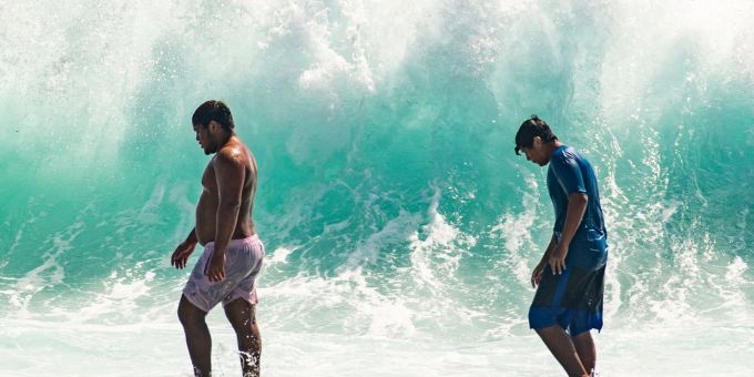 Zwei Männer vor einer hohen Brandung in Waikiki. Massive Wellen trafen an der Südküste Hawaiis auf Land. Zwei Männer vor einer hohen Brandung in Waikiki. Massive Wellen trafen an der Südküste Hawaiis auf Land.