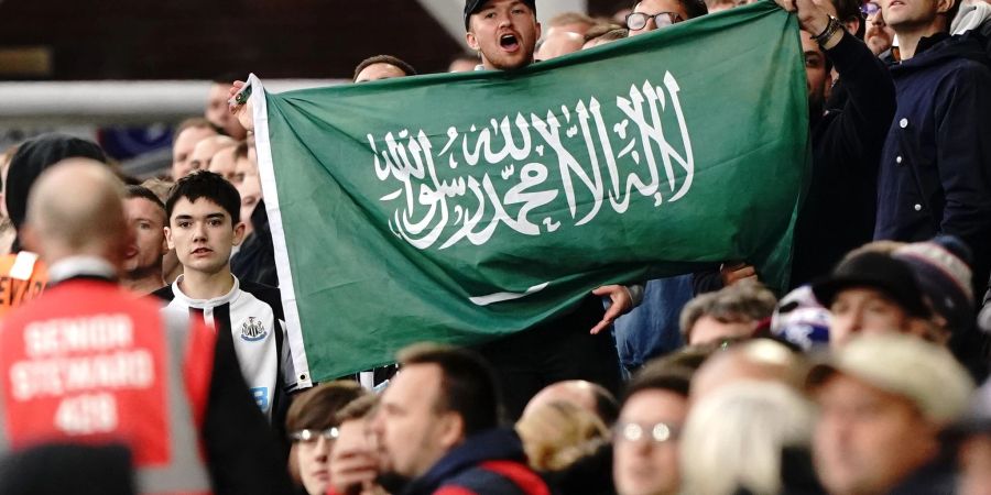 Ein Fan von Newcastle United hält die Fahne von Saudi-Arabien während eines Spiels hoch.