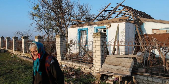 Eine ältere ukrainische Frau sammelt humanitäre Hilfsgüter vor ihrem Haus in einem Dorf, das durch militärische Auseinandersetzungen stark beschädigt wurde. ukraine krieg