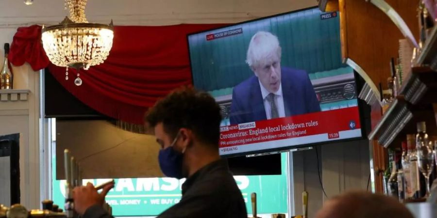 Ein Mitarbeiter eines Liverpooler Pubs schenkt Bier ein, während Premierminister Johnson im Hintergrund das neue Drei-Stufen-System erklärt. Foto: Peter Byrne/PA Wire/dpa