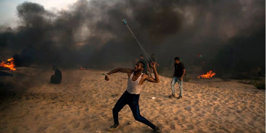 Ein palästinensischer Demonstrant schleudert einen Stein in Richtung israelischer Soldaten.