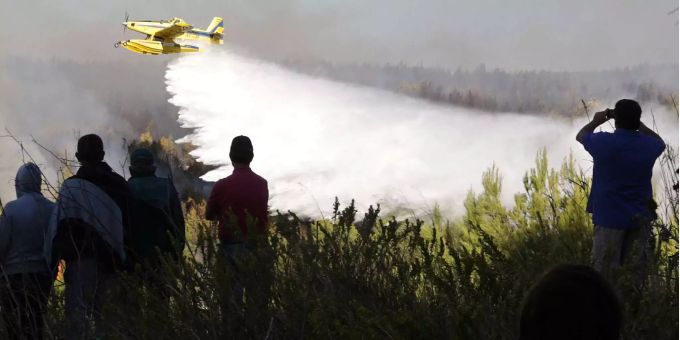 Einheimische beobachten, wie ein Löschflugzeug seine Ladung über einem brennenden Waldgebiet vor dem Dorf Charneca im Sintra-Nationalpark, westlich von Lissabon, abwirft. Einheimische beobachten, wie ein Löschflugzeug seine Ladung über einem brennenden Waldgebiet vor dem Dorf Charneca im Sintra-Nationalpark, westlich von Lissabon, abwirft.