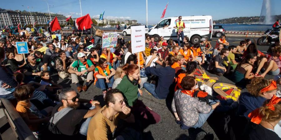 Tausende Demonstranten halten am Klima-Marsch sitzend auf der Pont du Mont Blanc in Genf Plakate hoch.