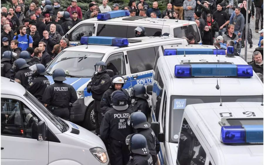 Teilnehmer der Demonstration von AfD und dem ausländerfeindlichen Bündnis Pegida, der sich auch die Teilnehmer der Kundgebung der rechtspopulistischen Bürgerbewegung Pro Chemnitz angeschlossen haben, ziehen zum Karl-Marx-Denkmal. Davor haben Polizisten ihre Wagen zu einer Sperre aufgestellt.