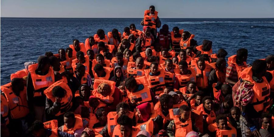 Mehrere Flüchtlinge aus verschiedenen afrikanischen Ländern sitzen vor der Küste von Libyen an Bord eines überfüllten Holzbootes.