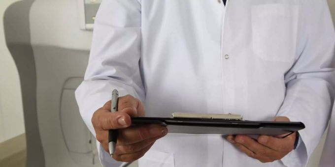 Ein Arzt hält ein Klemmbrett und einen Stift in der Hand. Arzt