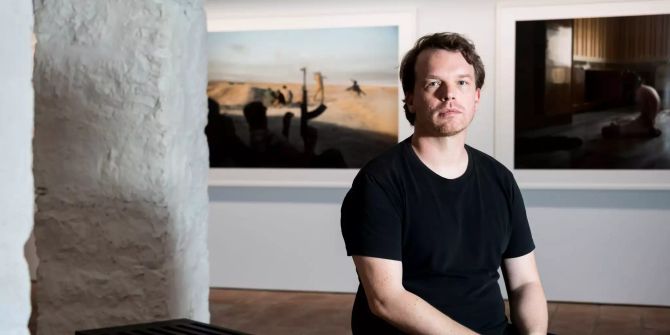 Der Schweizer Fotograph Matthias Bruggmann posiert vor seinen Kunstwerken.