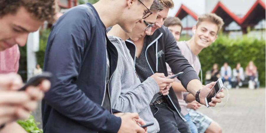 Eine Gruppe Gymnasiasten benutzen ihre Smartphone auf dem Pausenplatz ihrer Schule.