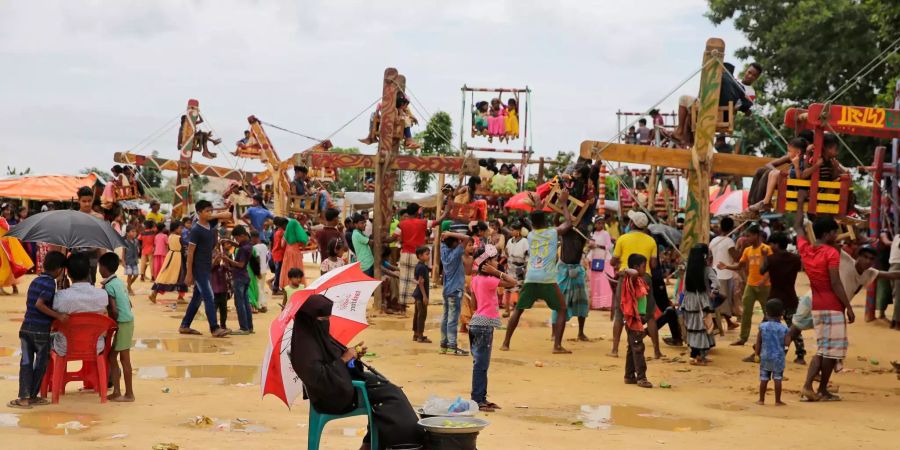 Eine Rohingya-Flüchtlingsfrau sitzt unter einem Schirm und verkauft neben einem Spielplatz in einem Rohingya-Flüchlingslager Früchte.