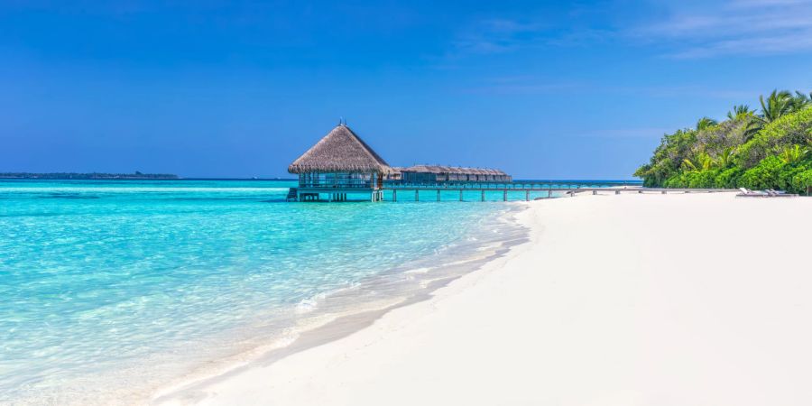 Blaues Meer mit Wasserbungalows am weissen Sandstrand.