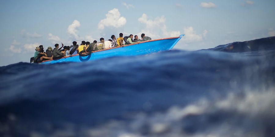 ARCHIV - Migranten sitzen in einem Holzboot im Mittelmeer nahe der Insel Lampedusa. (Archiv) Foto: Francisco Seco/AP/dpa