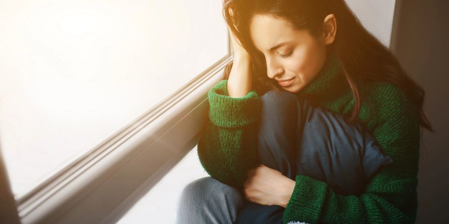 Frau sitzt traurig am Fenster