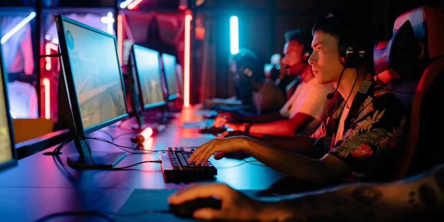 Mehrere Menschen sitzen in einem dunklen Raum vor ihren PCs und spielen Online-Games.