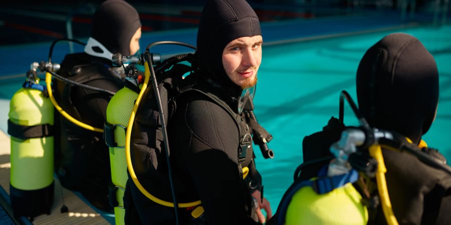 taucher mit Taucheranzug steht mit buddies vor schwimmbecken