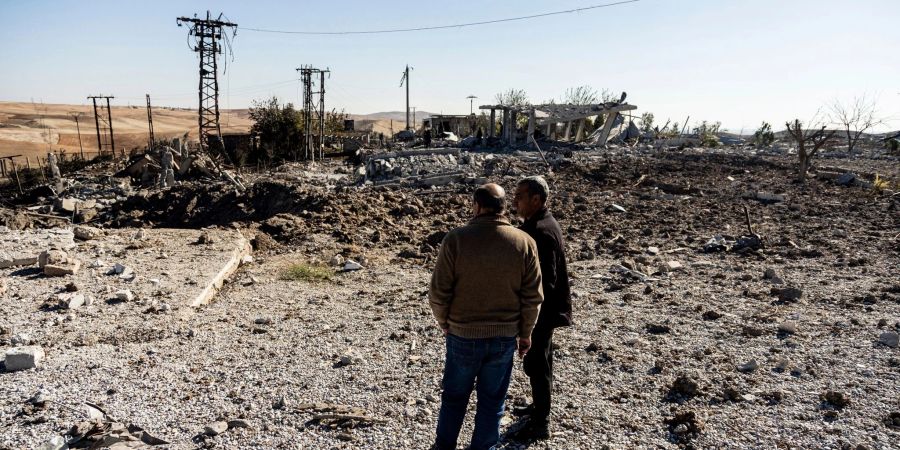 Zwei Männer begutachten Schäden in einem Gebiet um ein Elektrizitätswerk nach türkischen Luftangriffen.