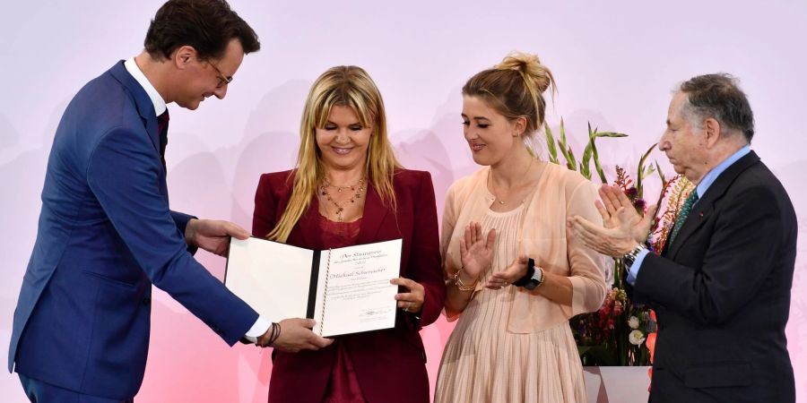 NRW-Ministerpräsident Hendrik Wüst (r) übergibt Corinna Schumacher und Tochter Gina die Auszeichnung - Ex-Ferrari-Teamchef Jean Todt (l) applaudiert.