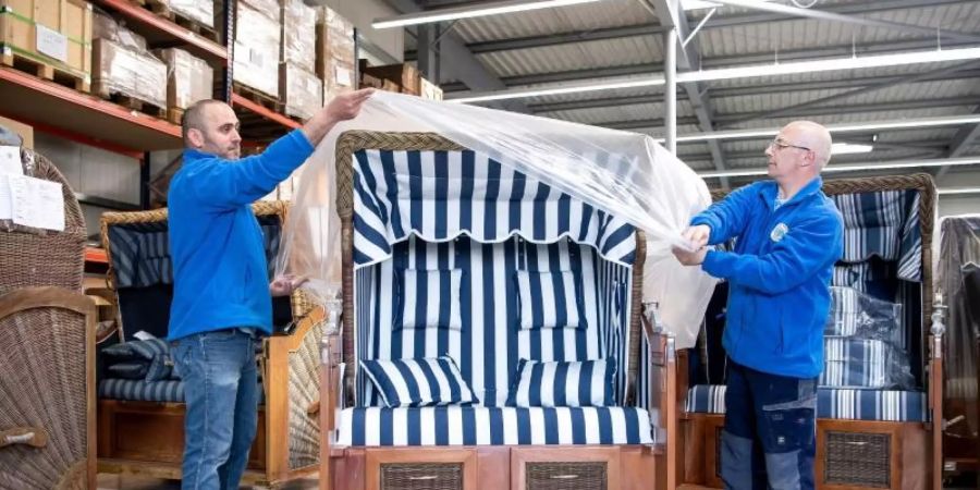 Zwei Arbeiter verpacken einen fertigen Strandkorb. Foto: Sina Schuldt/dpa