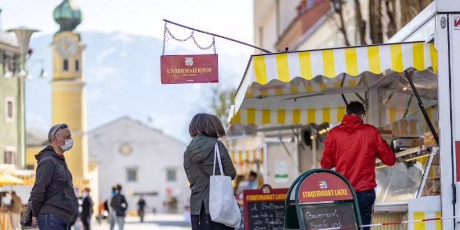 Menschen mit Mundschutz stehen an einem Marktstand in Lienz im Tirol an. Foto: Expa/ Johann Groder/APA/dpa